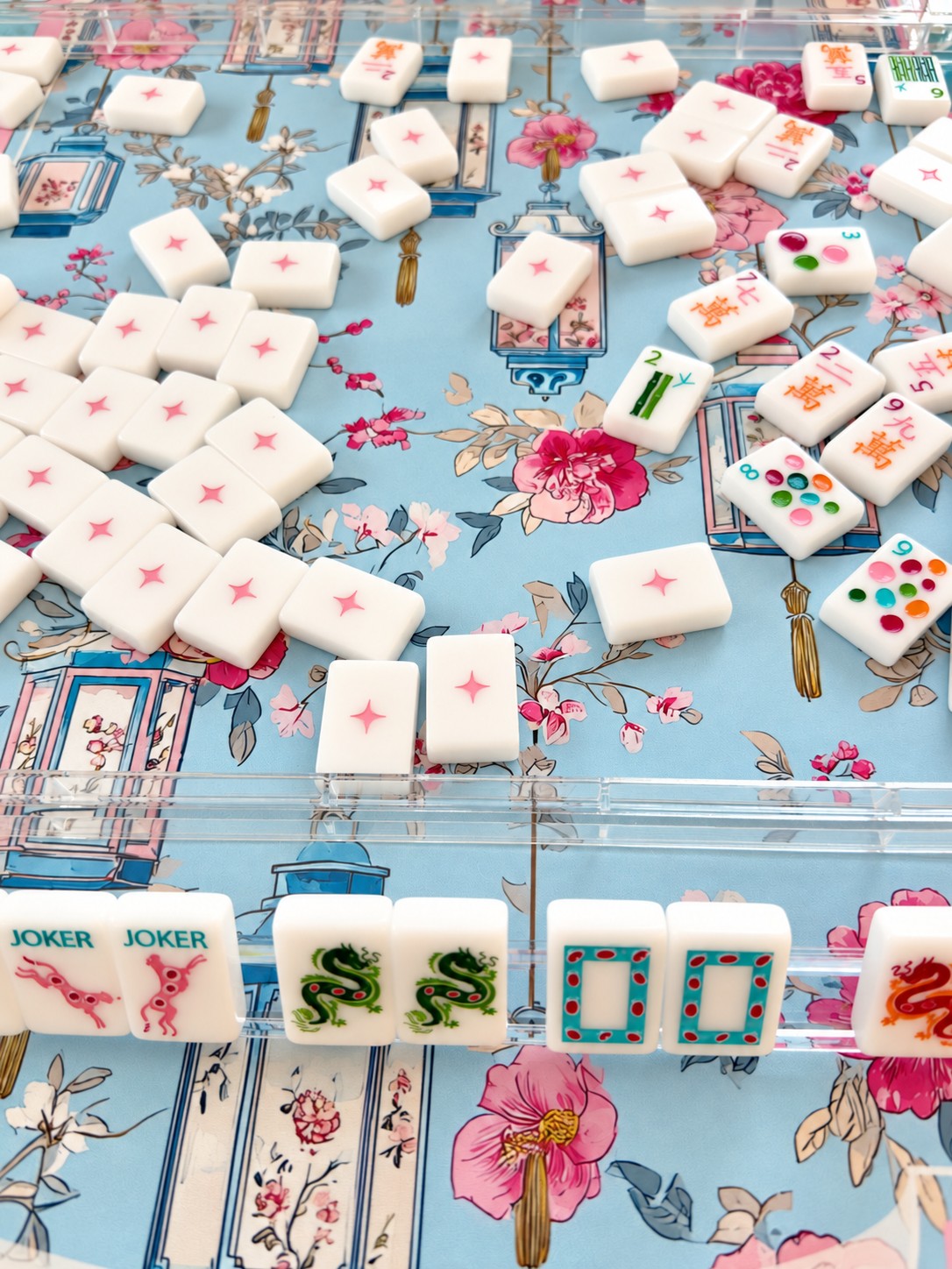 Mahjong tiles and racks on a colorful botanical playing mat
