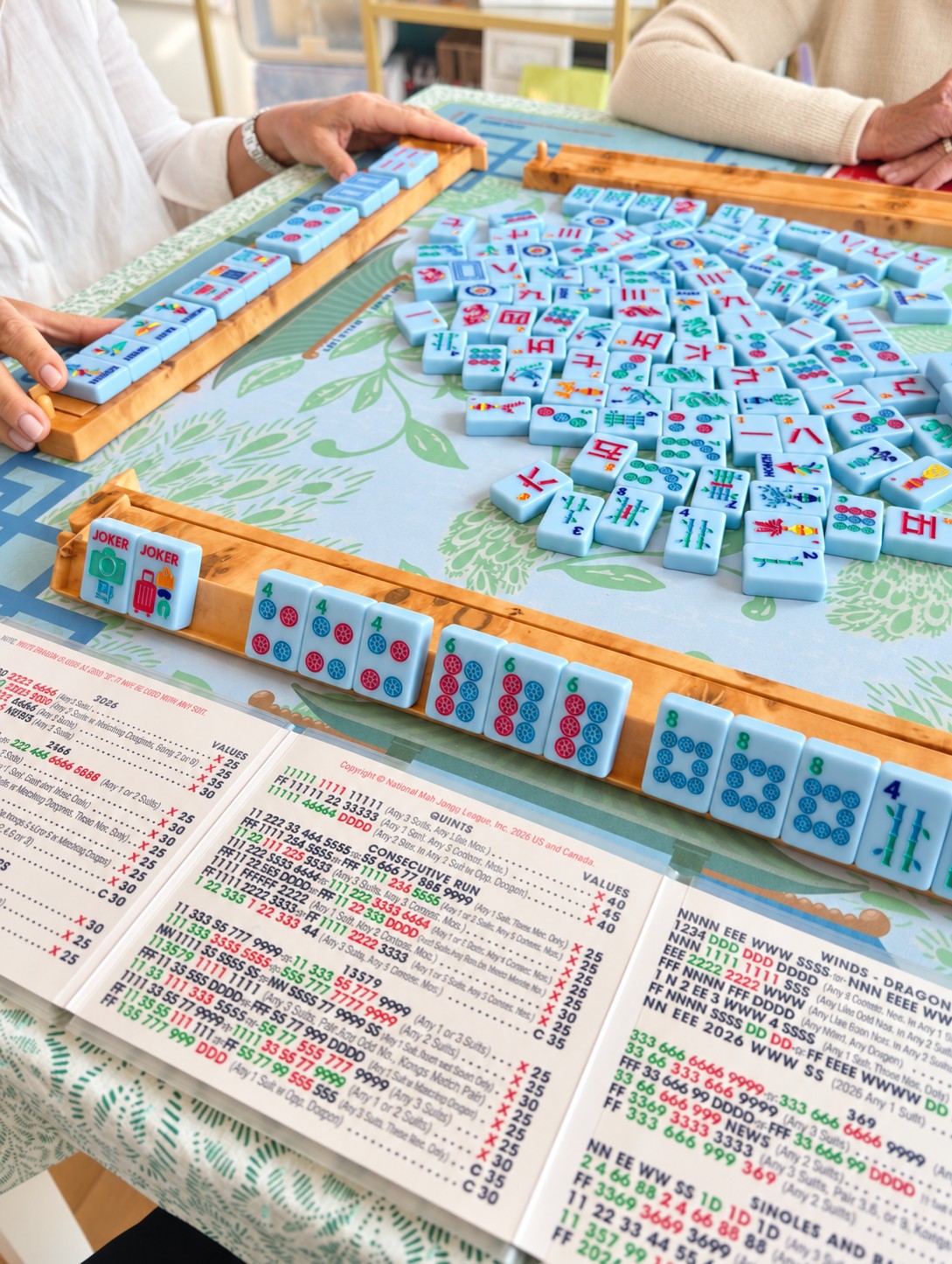 Mahjong tiles and racks on a colorful botanical playing mat